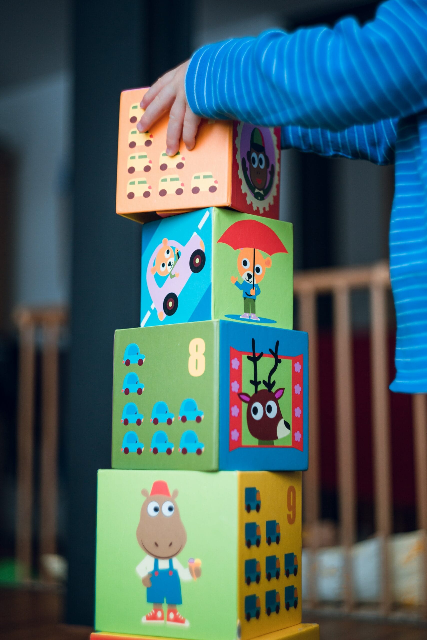 A child in a blue striped shirt stacks colorful illustrated blocks, each featuring cartoon animals, vehicles, and numbers—a fun activity often used in occupational therapy by allied health professionals to support development.